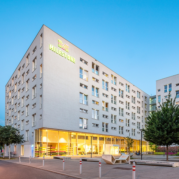 Das MILESTONE Vienna Prater ist in der Frontansicht zu sehen. Das Gebäude ist gräulich-weiß und an der oberen linken Ecke steht das Logo "MILESTONE".